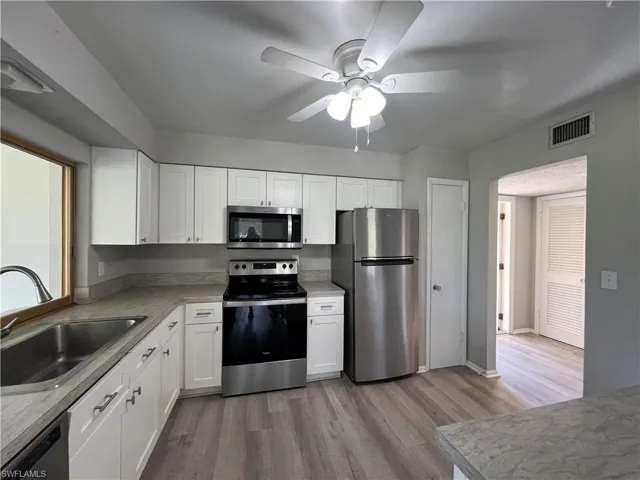 Kitchen with white cabinets, appliances with stainless steel finishes, ceiling fan, and light hardwood / wood-style flooring
