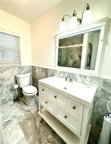 Bathroom with tile walls, a wainscoted wall, vanity, a marble finish shower, and light marble finish flooring
