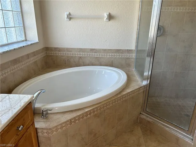 Bathroom with a stall shower, a garden tub, vanity, and a textured wall