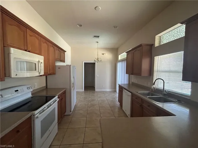 Kitchen featuring white appliances, suspended lighting, wood finish cabinetry, and light tile patterned floors