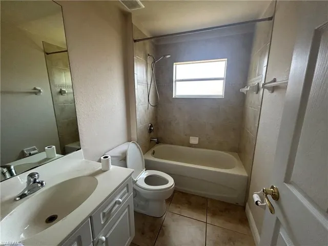 Full bathroom with vanity, bathing tub / shower combination, light tile patterned flooring, and a textured wall