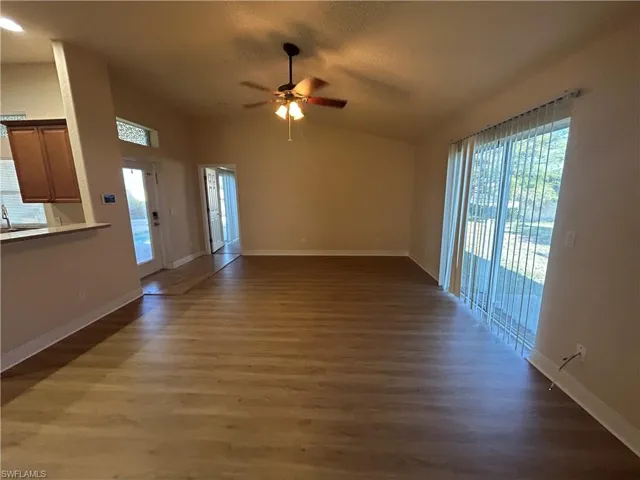 Unfurnished living room featuring a ceiling fan, dark wood-style flooring, healthy amount of natural light, and lofted ceiling