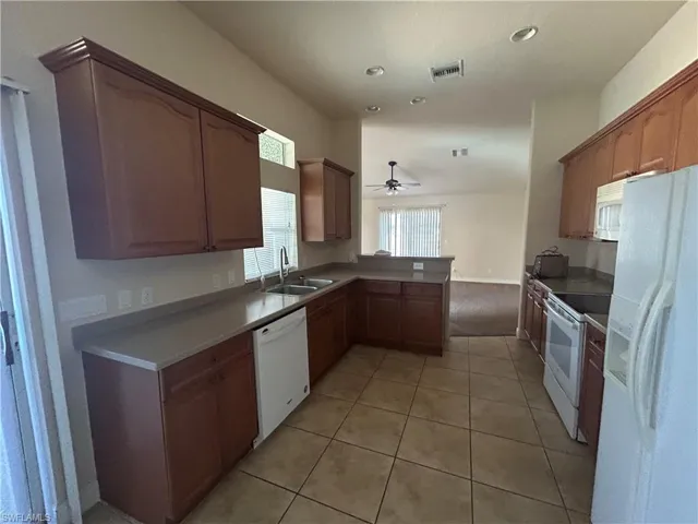 Kitchen featuring white appliances, light tile patterned floors, a ceiling fan, wood finish cabinets, and a peninsula