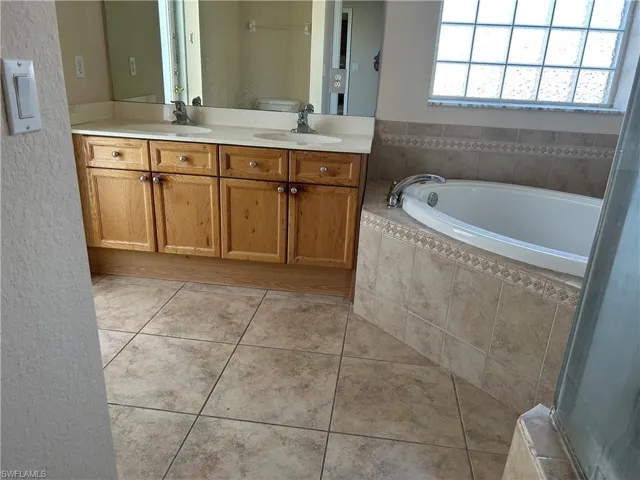 Bathroom with double vanity, a garden tub, light tile patterned flooring, and a textured wall