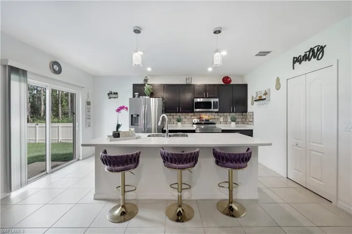Kitchen with a center island with sink, pendant lighting, stainless steel appliances, and tasteful backsplash