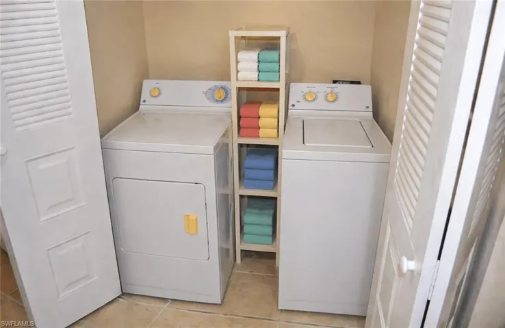 Dedicated laundry closet featuring a white washer and dryer set, neutral wall color, tiled flooring, and white louvered bifold doors