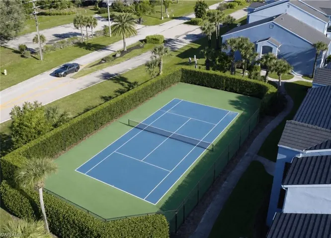 Full-size tennis court featuring a blue playing surface with white lines, surrounded by a green perimeter