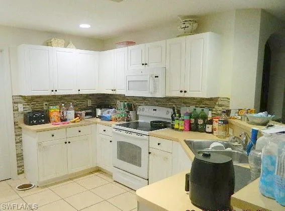 Kitchen featuring white appliances, white cabinets, light countertops, light tile patterned flooring, and backsplash