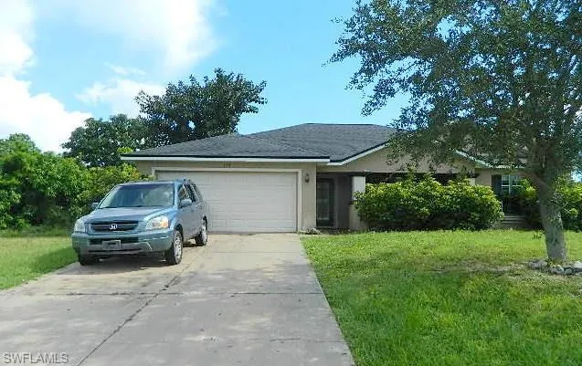 Single story home featuring a garage, driveway, a front lawn, and stucco siding