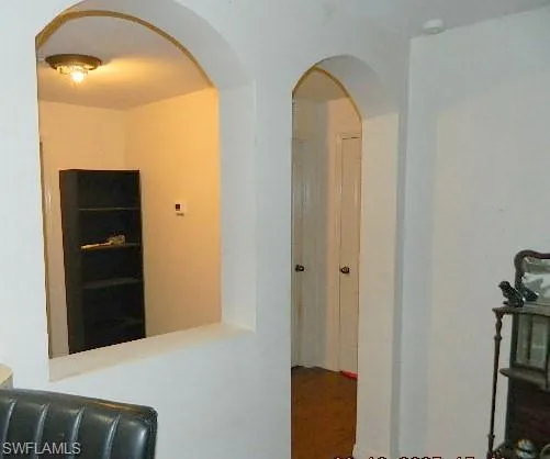 Hallway featuring arched walkways and wood finished floors