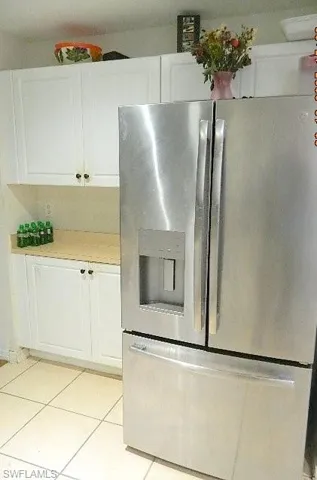 Kitchen featuring stainless steel fridge, white cabinetry, light tile patterned floors, and light countertops