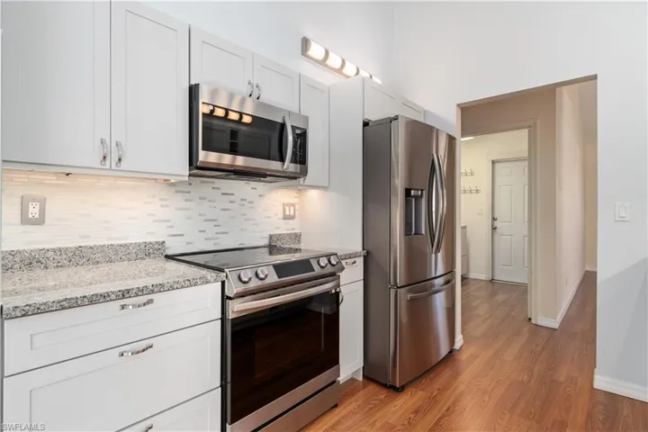 Kitchen with backsplash, light stone countertops, light wood-type flooring, appliances with stainless steel finishes, and white cabinetry