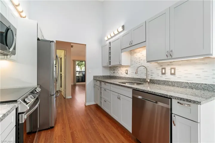 Kitchen featuring sink, stainless steel appliances, light stone counters, light hardwood / wood-style flooring, and decorative backsplash