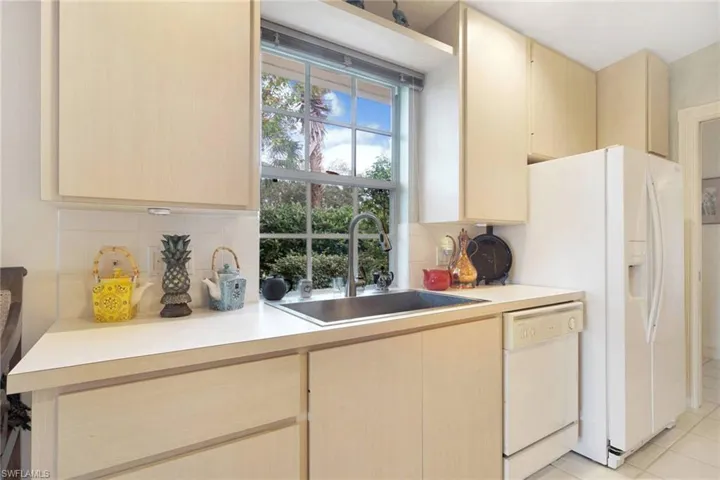 Kitchen with dishwasher, light brown cabinets, sink, tasteful backsplash, and light tile patterned floors