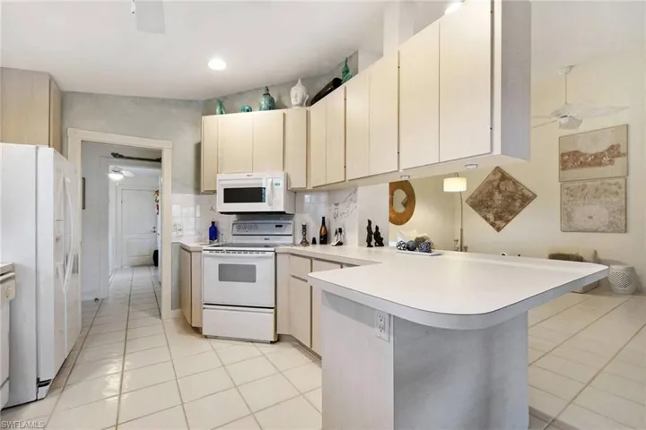 Kitchen with a breakfast bar, white appliances, light tile patterned floors, tasteful backsplash, and kitchen peninsula