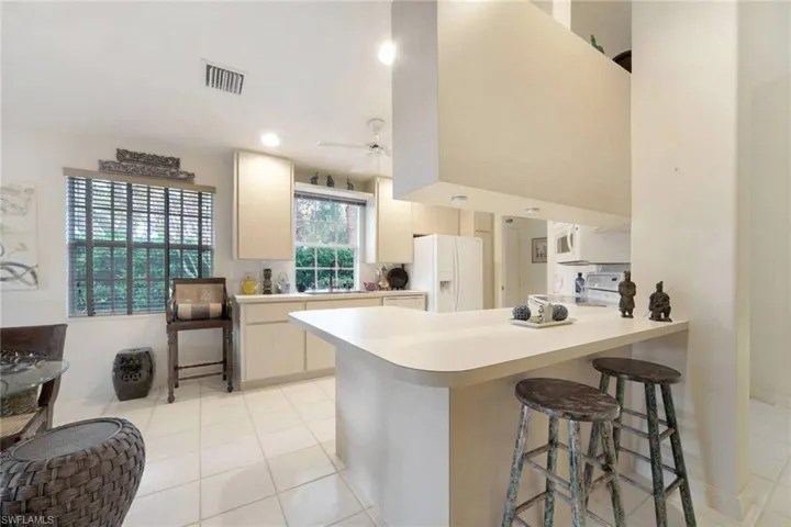 Kitchen featuring ceiling fan, kitchen peninsula, white appliances, a breakfast bar, and light tile patterned floors