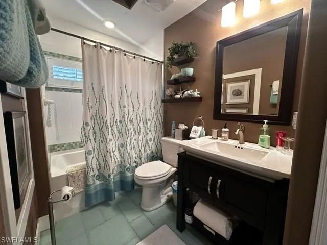 Bathroom with tile patterned floors, shower / bath combination with curtain, vanity, and toilet