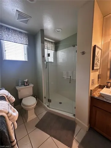 Bathroom featuring toilet, a stall shower, visible vents, tile patterned flooring, and vanity