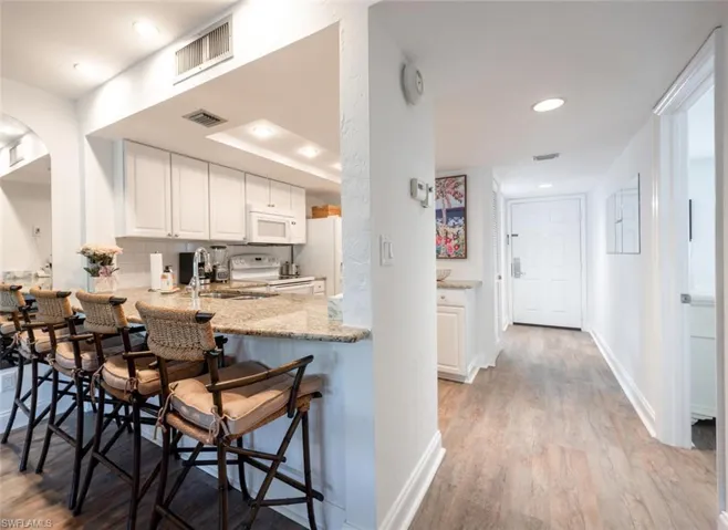 Kitchen featuring white appliances, sink, white cabinetry, light hardwood / wood-style floors, and a breakfast bar area