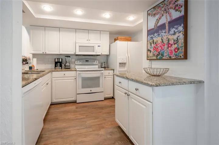 Kitchen with light hardwood / wood-style floors, white cabinetry, tasteful backsplash, and white appliances