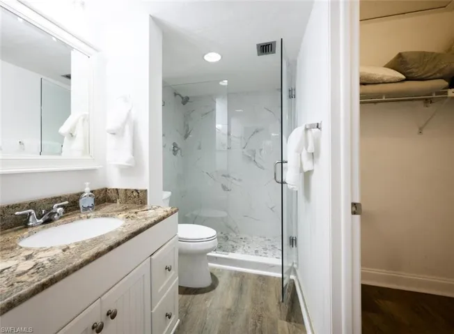 Bathroom with vanity, a shower with shower door, wood-type flooring, and toilet