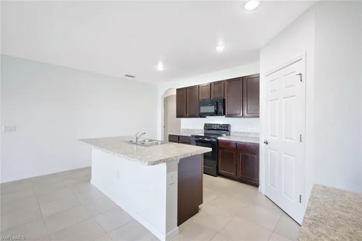 Kitchen with sink, dark brown cabinetry, black appliances, an island with sink, and light tile patterned flooring