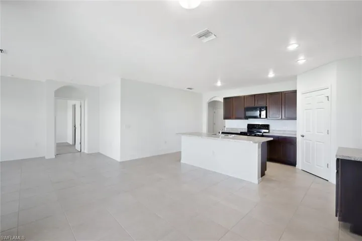 Kitchen with dark brown cabinetry, sink, an island with sink, light stone countertops, and black appliances