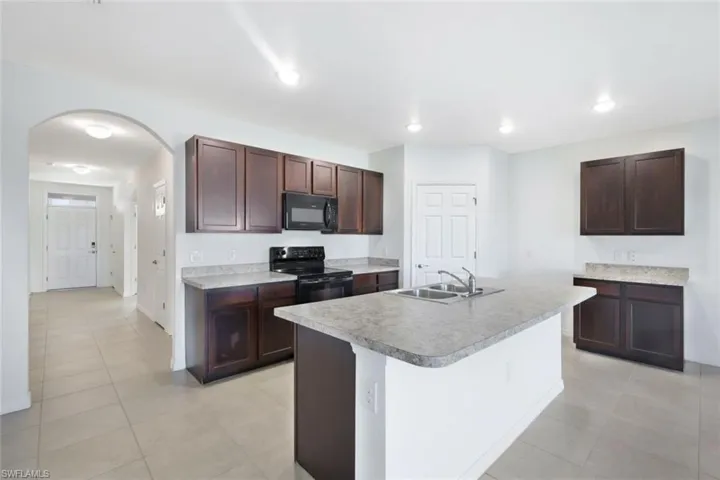 Kitchen featuring dark brown cabinetry, sink, light tile patterned floors, an island with sink, and black appliances