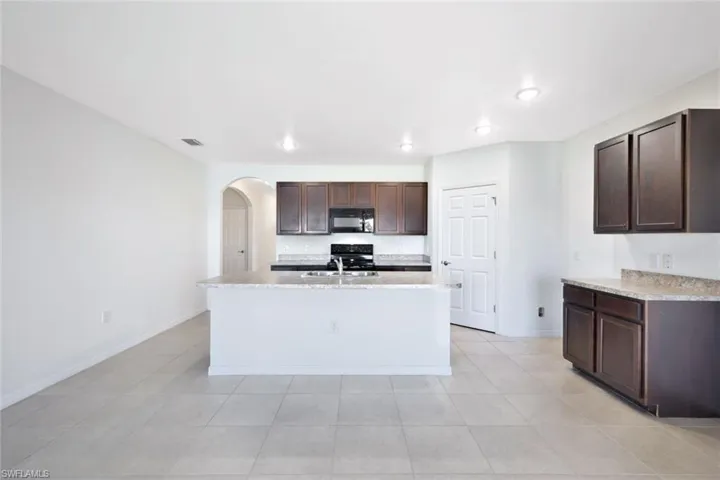 Kitchen with electric stove, sink, light tile patterned floors, a kitchen island with sink, and dark brown cabinetry