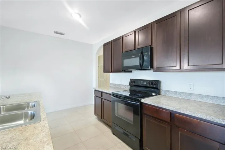 Kitchen with dark brown cabinets, sink, light tile patterned floors, and black appliances