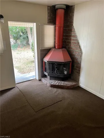 Unfurnished living room featuring carpet flooring and a wood stove