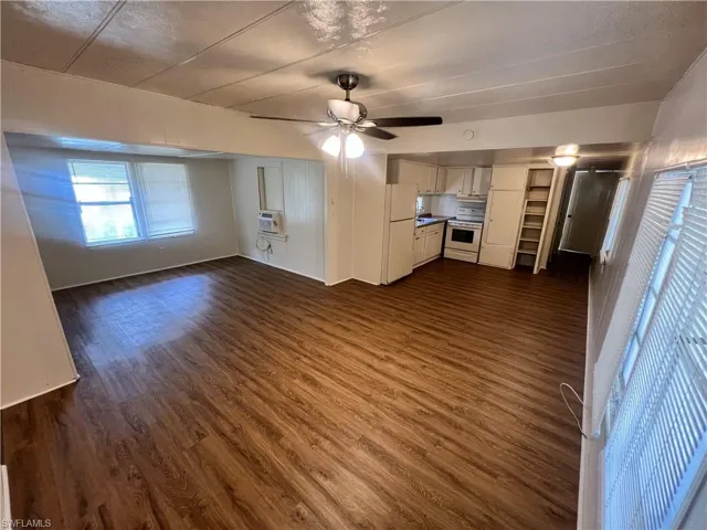 Unfurnished living room with a wall mounted AC, dark wood-type flooring, and ceiling fan