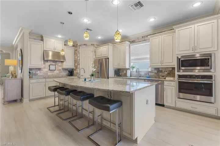 Kitchen featuring off-white cabinetry, stone-finish countertops, stainless steel appliances, a textured stone backsplash, and recessed lighting