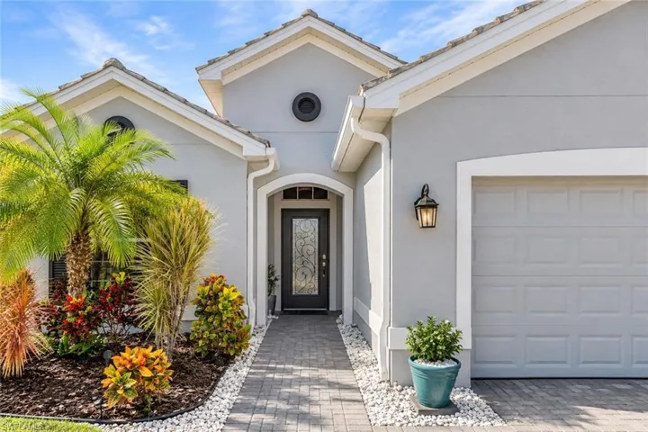 Stucco exterior featuring a paver walkway, decorative glass-insert front door, arched entryway, and multi-gabled roofline