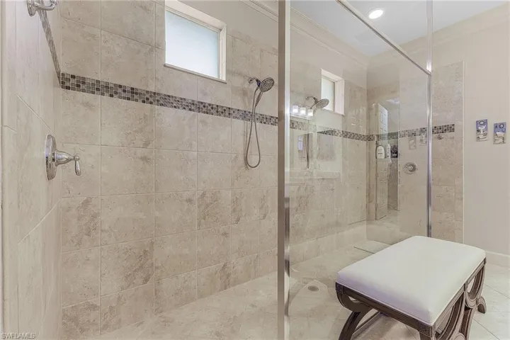 Walk-in shower featuring floor-to-ceiling stone tile, a glass enclosure, dual shower heads, and decorative tile inlay