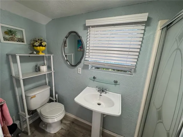 Bathroom featuring a shower with door, vaulted ceiling, hardwood / wood-style flooring, toilet, and a textured ceiling