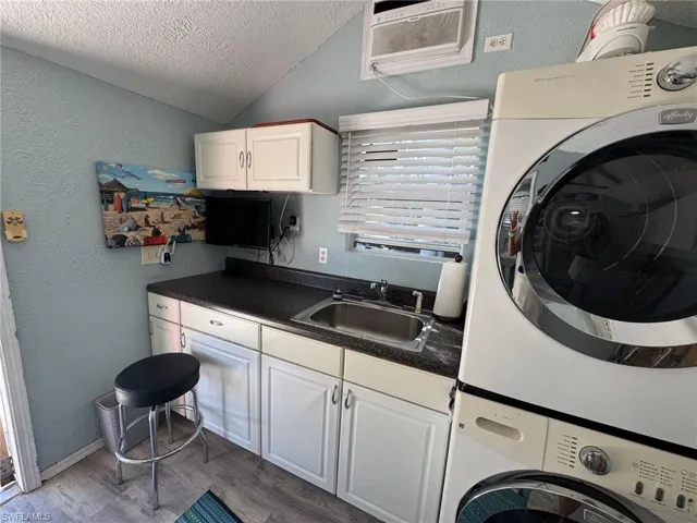 Kitchen featuring stacked washing maching and dryer, white cabinetry, lofted ceiling, and sink