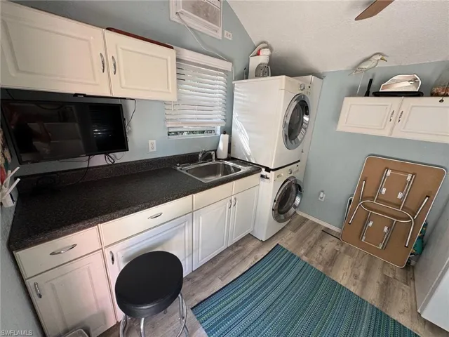 Washroom featuring a textured ceiling, light wood-type flooring, sink, and stacked washer and clothes dryer