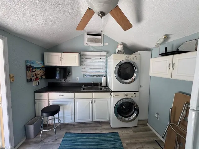 Laundry area featuring dark hardwood / wood-style flooring, a textured ceiling, ceiling fan, sink, and stacked washer and clothes dryer