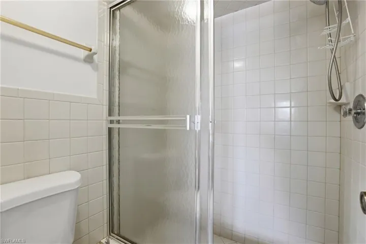 Glass-enclosed shower with white square tile walls and a chrome shower fixture