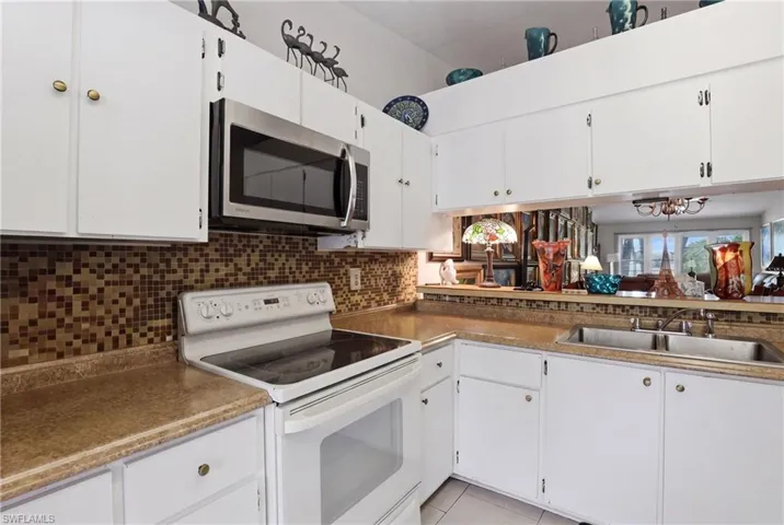 Kitchen featuring white cabinetry, a stainless steel over-the-range microwave, a white electric range, mosaic tile backsplash, and a double basin sink