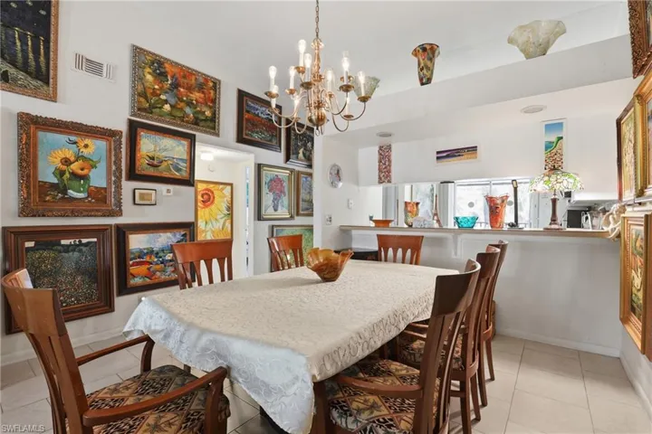 Dining area featuring a brass chandelier, tile flooring, and a pass-through counter opening