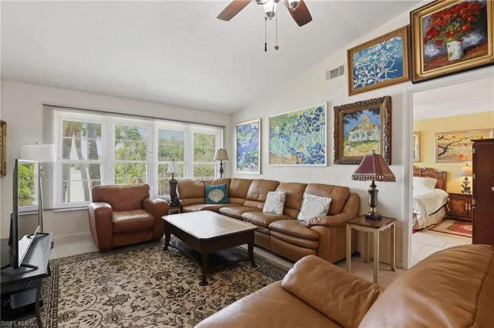 Vaulted ceiling living area featuring multiple windows, a ceiling fan, and a neutral color palette
