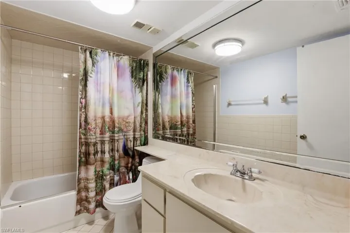 Bathroom featuring a large vanity with an integrated sink, an expansive wall-mounted mirror, a toilet, and a combination shower/bathtub with tile surround