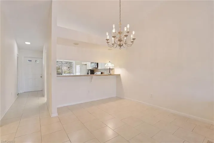 Open-concept dining area featuring a multi-bulb chandelier, tile flooring, and a pass-through counter to the kitchen