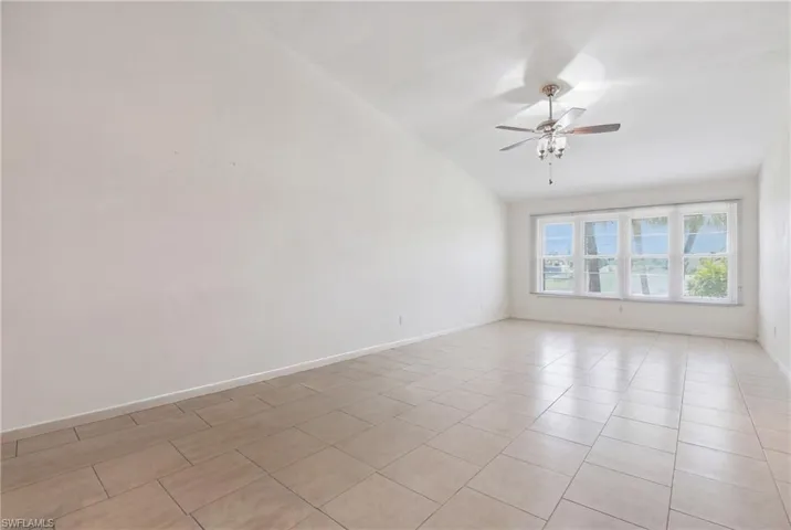 Spacious room featuring light-toned tile flooring, white baseboards, and a contemporary ceiling fan with integrated lighting