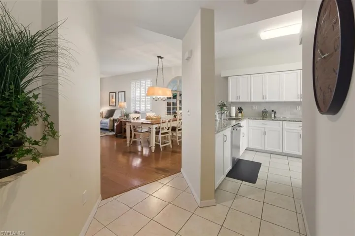 Kitchen with light tile patterned flooring, white cabinets, light stone countertops, backsplash, and hanging light fixtures