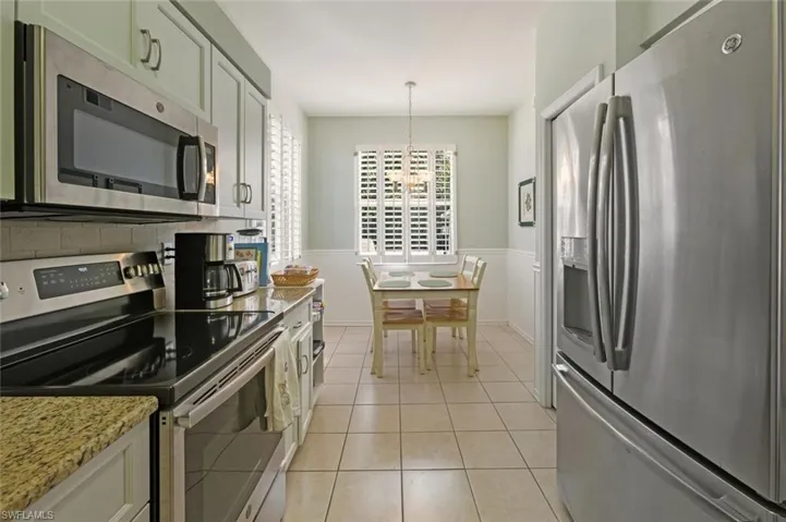 Kitchen featuring stainless steel appliances, light tile patterned floors, hanging light fixtures, a chandelier, and light stone counters