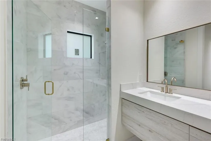 Full shower featuring a marble finish and custom built vanity.