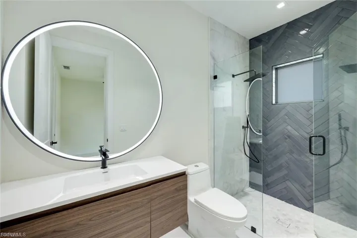 This en-suite bath features elegant marble shower tiles and a modern LED mirror, adding a touch of luxury and style to the guest bedroom, while offering both comfort and convenience.